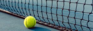 close-up of a fluorescent yellow ball on blue acrylic surface in front of the net of a modern professional tennis court
