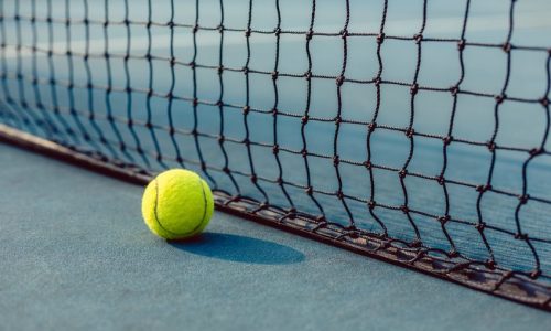 close-up of a fluorescent yellow ball on blue acrylic surface in front of the net of a modern professional tennis court
