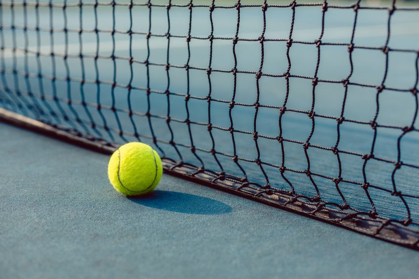 close-up of a fluorescent yellow ball on blue acrylic surface in front of the net of a modern professional tennis court